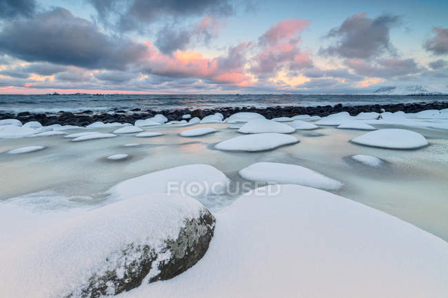 Amanecer en el mar frío rodeado de rocas nevadas con forma de viento y hielo en Eggum Vestvag landscapey Island, Islas Lofoten, Noruega, Europa - foto de stock