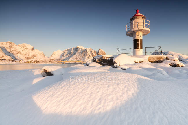 Der Leuchtturm umgeben von Schnee umrahmt die schneebedeckten Gipfel und das gefrorene Meer reine Nordland, erhabene Inseln, Norwegen, Europa — Stockfoto