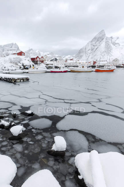 Mar helado y picos nevados alrededor de las casas típicas llamadas rorbu y barcos de pesca Hamn paisaje, Islas Lofoten, Norte de Noruega, Europa - foto de stock
