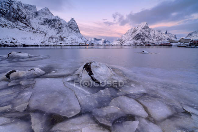 Los colores rosados de la puesta del sol y el mar congelado rodean los pueblos pesqueros Reine Nordland, Islas Lofoten paisaje, Noruega, Europa - foto de stock
