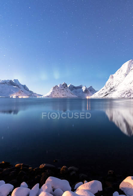 The snowy peaks are reflected in the frozen sea on a starry winter night Reine Bay Nordland mountain landscape, Lofoten Islands, Norway, Europe — Stock Photo