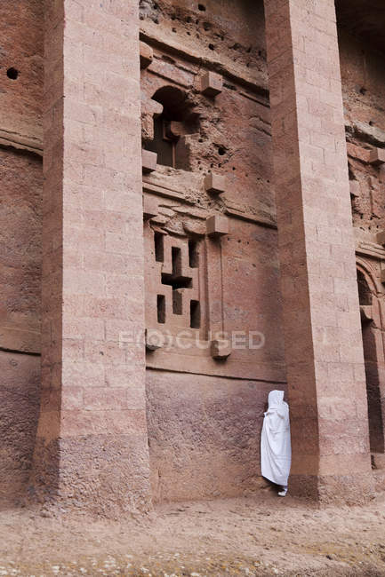 The rock-hewn churches of Lalibela in Ethiopia. Pilgrim praying in front of a church.  The churches of Lalibela have been constructed in the 12th or 13th century. They have been hewn from the solid rock and are considered to be one of the largest mon — Stock Photo