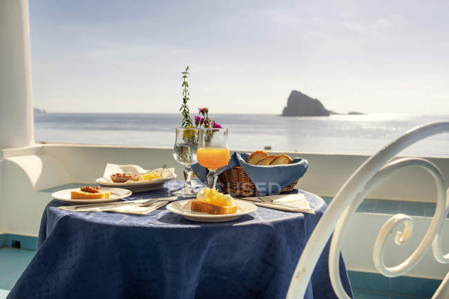 Desayuno típico siciliano con mermeladas caseras y zumo de naranja fresco y vista desde la isla de Panarea - foto de stock