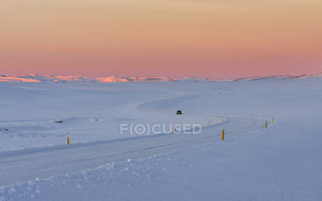 Einsame Landstraße bei Sonnenaufgang in den schneebedeckten Bergen Islands. europa, nordeuropa, island, februar — Stockfoto