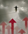 Man walking tightrope over arrows in cloudy sky — Stock Photo