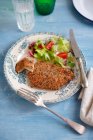 Chuleta de pollo crujiente con semillas de chía y ensalada de verduras servida en plato sobre mesa de madera azul - foto de stock
