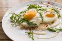 Uova fritte sopra formaggio fresco con rucola su piatto bianco — Foto stock
