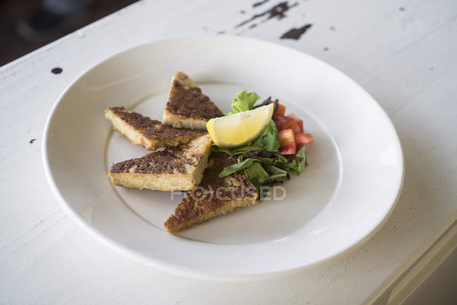 Dreiecksscheiben Cecina-Kuchen mit Kartoffeln und Zwiebeln serviert mit Gemüse und Zitronenstück. — Stockfoto