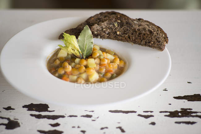 Chickpeas and vegetables soup served with bread slices. — Stock Photo