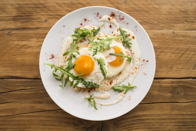 Fried eggs over cream cheese with arugula on white plate, top view — Stock Photo
