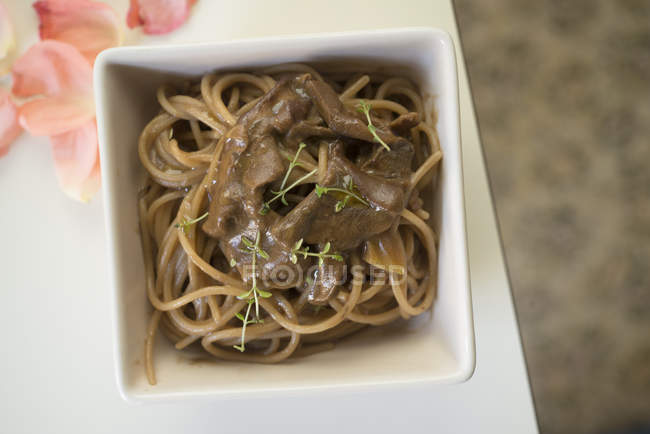 Spaghetti with semi-whole mushrooms and thyme in square bowl, top view. — Stock Photo