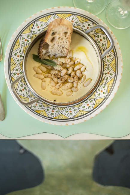 Top view of plate with cream of cannellini beans, goat cheese and sage, served with slice of bread. — Stock Photo