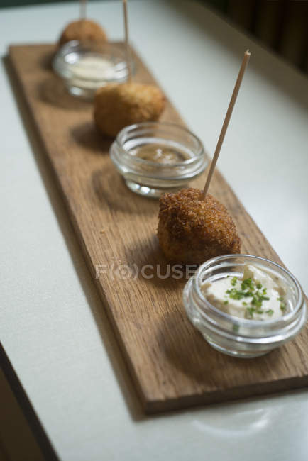 Kartoffel- und Quinoa-Bällchen serviert mit Bögen aus drei Saucen auf Holzbrett. — Stockfoto