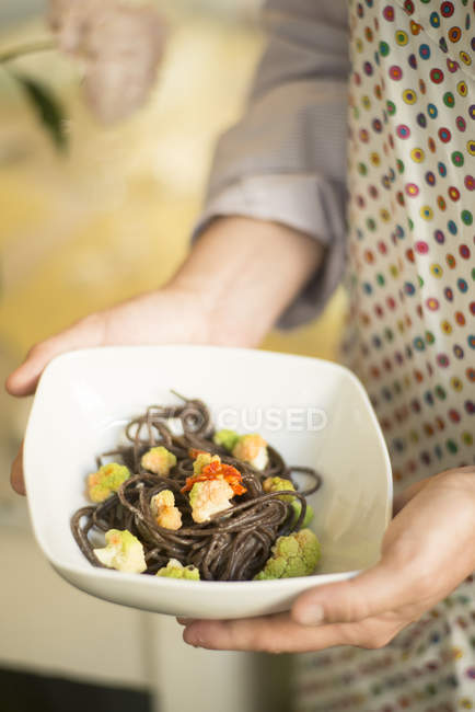 Female chef carrying bowl of buckwheat noodles with spicy cauliflower and vegetables. — Stock Photo