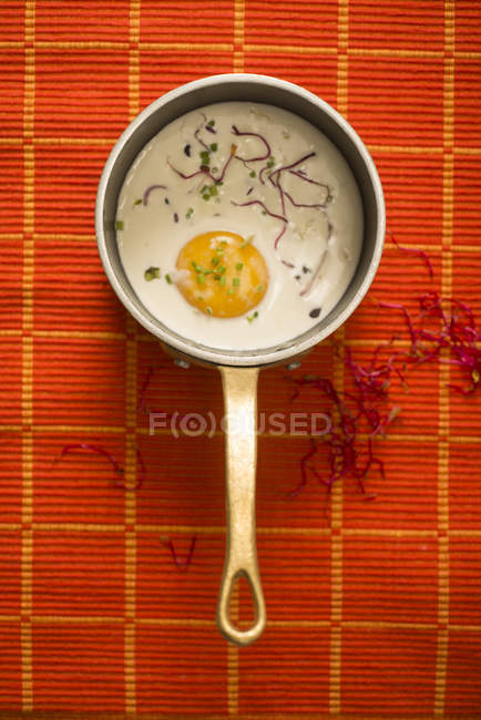 Top view of pan with poached egg with green sprouts on red table. — Stock Photo