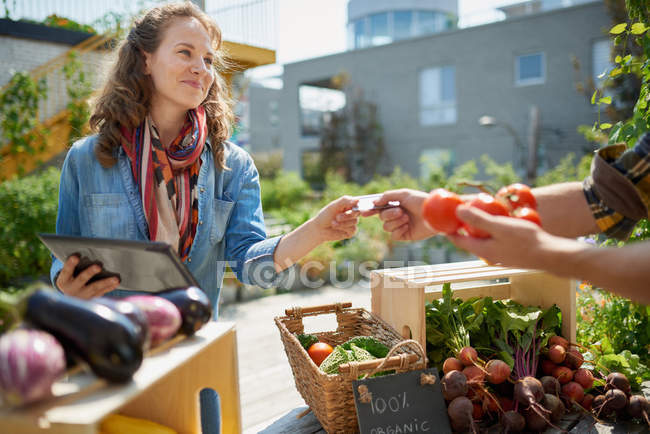 Femme amicale entretenant un étal de légumes biologiques à un marché de producteurs et vendant des légumes frais du jardin sur le toit — Photo de stock