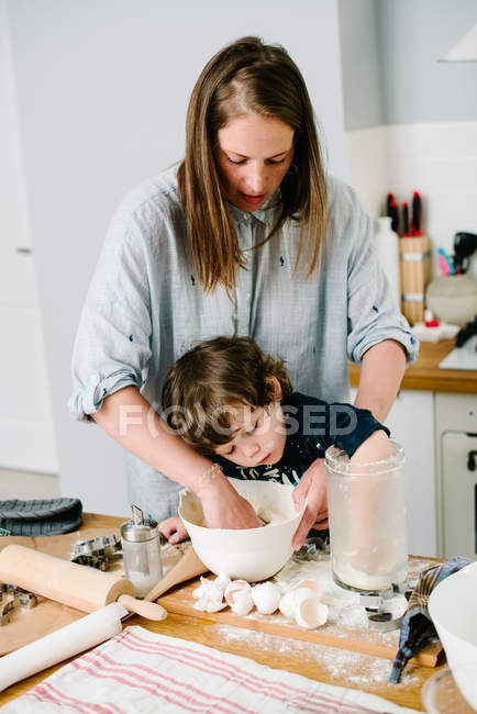 Ragazzino aiutando sua madre con la cottura in cucina sta — Foto stock