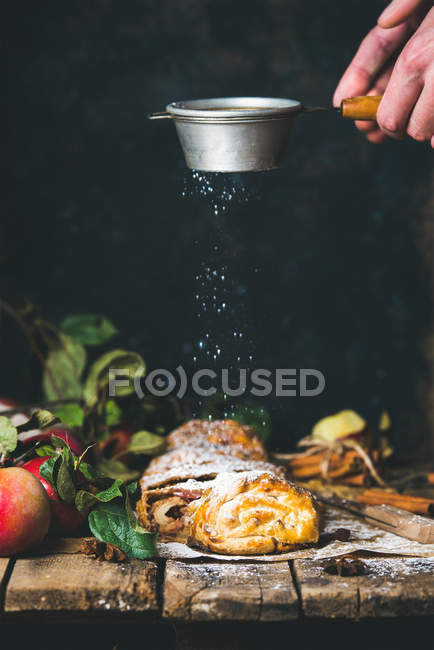 Les mains de l'homme saupoudrer de sucre en poudre sur le gâteau strudel pomme — Photo de stock