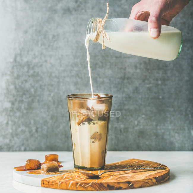 Die Hand des Mannes gießt Milch in eiskalten Latte — Stockfoto