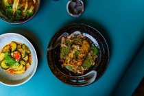 Вид зверху на їжу в азіатському стилі, смачні східні страви в мисках на синьому фоні — стокове фото