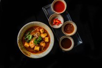 Vista superior de sopa deliciosa e tigelas com ingredientes e molhos em fundo preto — Fotografia de Stock