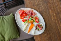Верхний вид тарелки с различными сырами, ветчиной, салями, брускеттой и овощами — стоковое фото