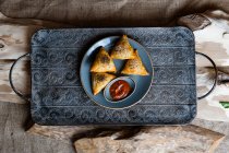 Вид сверху на свежие вкусные треугольные булочки с семенами и соусом на тарелке — стоковое фото