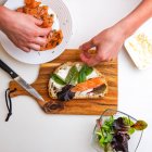 Вид на жіночі руки, які готують брушетта з лососем, помідорами та овочами на білому тлі — стокове фото