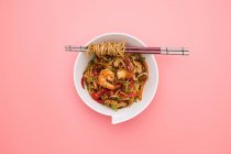 Chinese noodles with shrimps and vegetables on pink background — Stock Photo