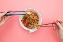 Китайская лапша с креветками и овощами на розовом фоне — стоковое фото