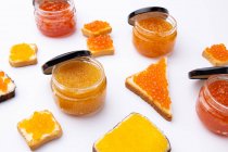 Bocaux de caviar rouge et des toasts avec du beurre et différents types de caviar rouge sur le fond blanc — Photo de stock