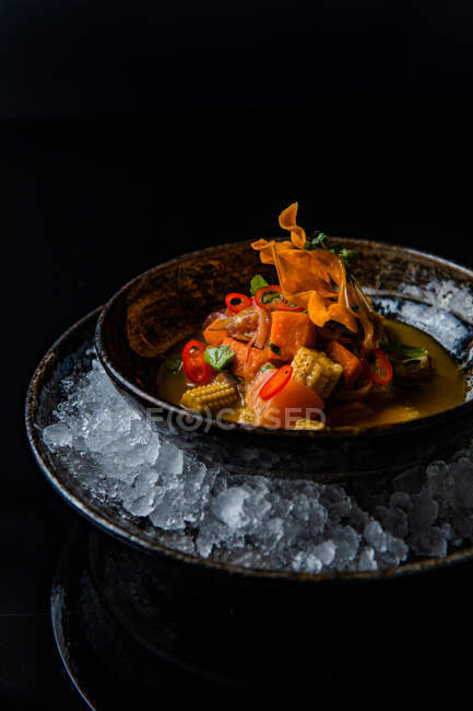 Close-up view of delicious meal with fried vegetables in bowl of ice cubes on black background — Stock Photo