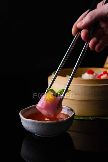 Tiro recortado de la persona sosteniendo palillos y comiendo deliciosa comida tradicional china - foto de stock