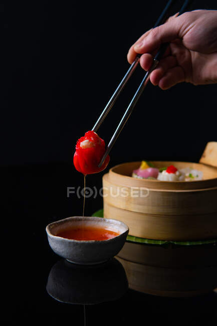 Tiro recortado de la persona sosteniendo palillos y comiendo deliciosa comida tradicional china - foto de stock