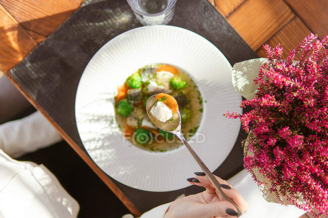 Plan recadré de femme mangeant une délicieuse soupe saine avec des légumes dans une assiette blanche — Photo de stock