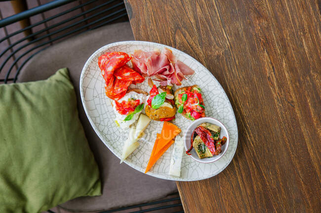 Top view of plate with various cheeses, ham, salami, bruschetta and vegetables — Stock Photo