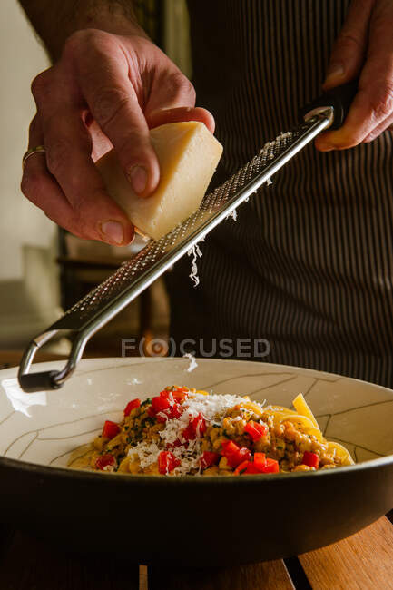 Recortado tiro de persona rallando queso parmesano por encima del plato con deliciosa pasta - foto de stock