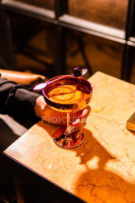 Обрезанный снимок женщины, держащей стакан коктейля, сидя за мраморным столом — стоковое фото