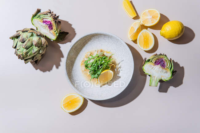 Vista superior de ensalada fresca con limones y alcachofas verdes sobre fondo blanco - foto de stock
