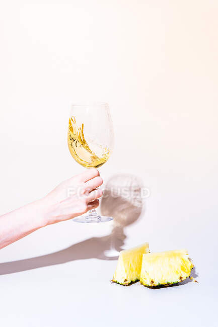 Cropped shot of woman holding wine glass, sliced pineapple on light background — Stock Photo