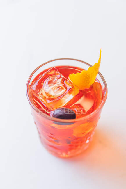 Vaso de cóctel rojo con zumo de frutas y cubitos de hielo sobre fondo blanco - foto de stock
