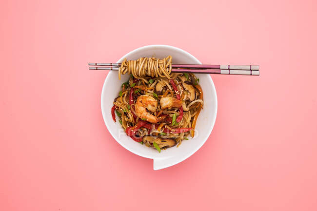Китайська локшина з креветками та овочами на рожевому фоні. — стокове фото