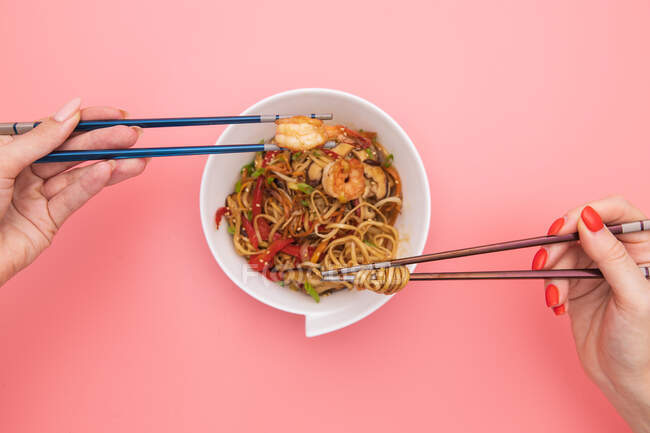 Chinese noodles with shrimps and vegetables on pink background — Stock Photo