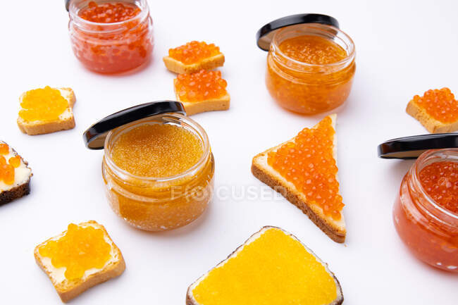 Jarros de caviar vermelho e torradas com manteiga e diferentes tipos de caviar vermelho no fundo branco — Fotografia de Stock