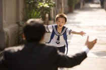 Chinese schoolboy running towards father on street — Stock Photo