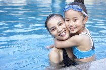 Madre e hija china abrazándose en la piscina - foto de stock