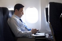 Uomo d'affari cinese che lavora con smartphone in aereo — Foto stock