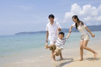 Genitori che tengono il figlio dondolante sulla spiaggia — Foto stock