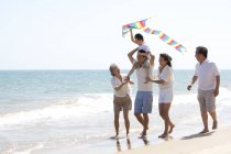 Menino chinês com pipa nos ombros do pai andando com a família na praia — Fotografia de Stock
