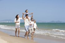 Fille chinoise sur les épaules du père marchant avec la famille sur la plage — Photo de stock